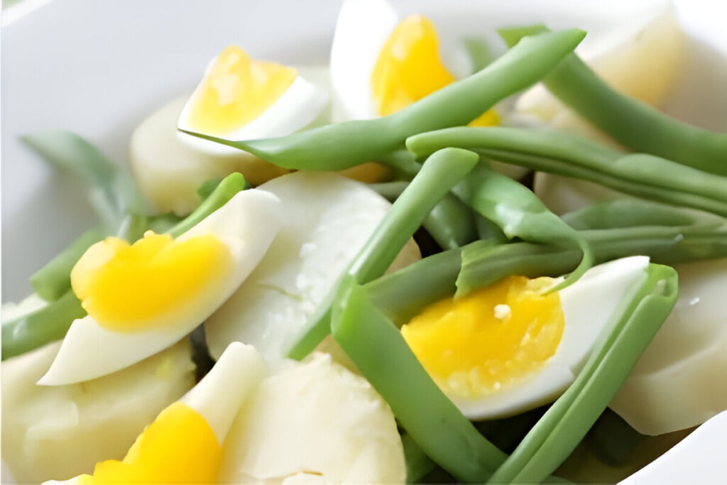 Ensalada de chauchas con huevo duro, cebolla y tomate servida en plato blanco