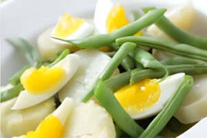 Ensalada de chauchas con huevo duro, cebolla y tomate servida en plato blanco