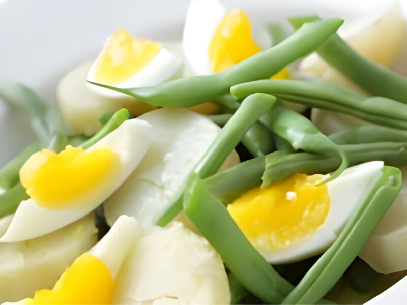 Ensalada de chauchas con huevo duro, cebolla y tomate servida en plato blanco