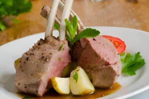 Plato de cordero a la menta servido con salsa verde y guarnición de verduras asadas