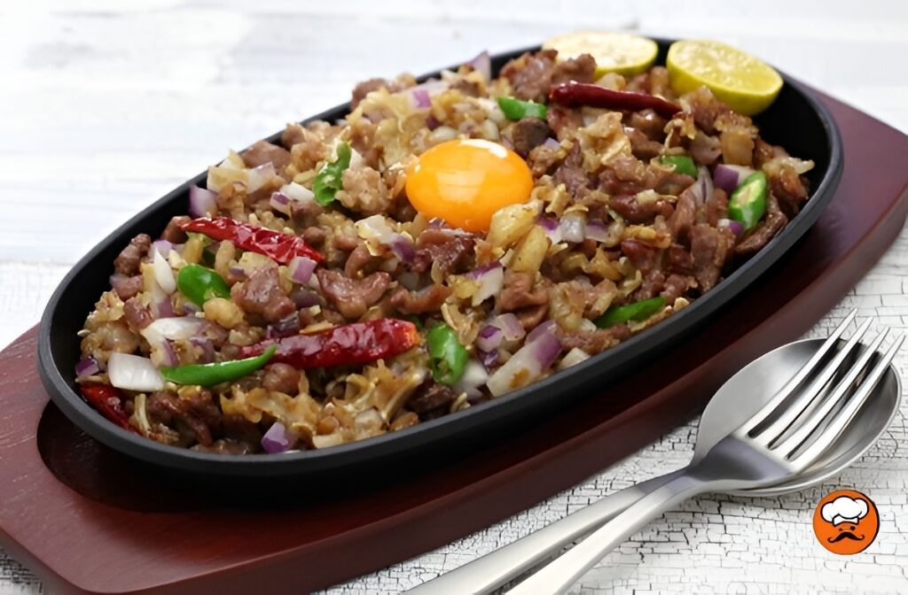 Sisig de cerdo filipino servido chisporroteante con huevo y calamansi