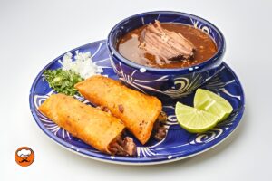 Tacos de birria mexicana con carne desmenuzada y consomé caliente
