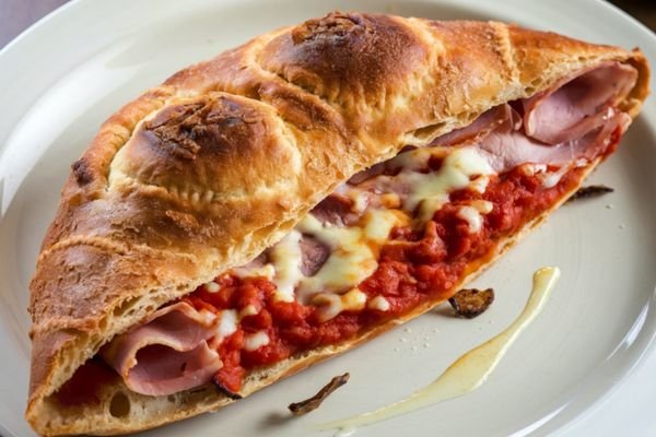 Calzone italiano horneado con masa dorada, queso fundido, salsa de tomate y jamón.