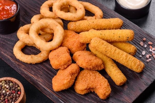 Aperitivos fritos crujientes con aros de cebolla, bocados rebozados y salsas para acompañar.