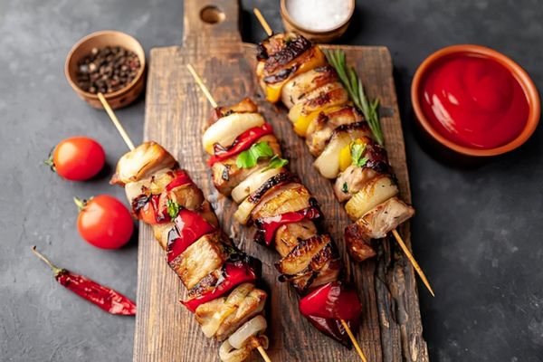 Brochetas a la parrilla con carne, pimientos y cebolla asados sobre una tabla de madera.