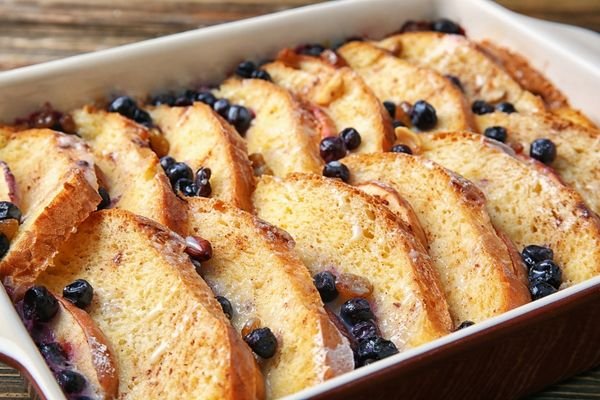 Receta de Budínes de pan al horno con rebanadas doradas y pequeños frutos oscuros.