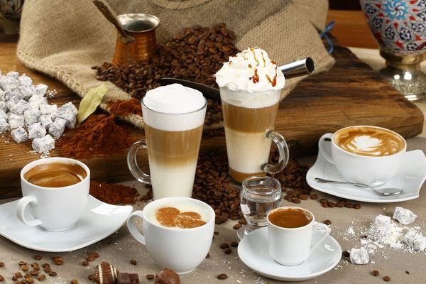 Variedades de café en tazas y vasos, con espuma de leche, granos de café y cacao.