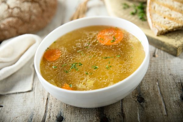 recetas de Caldo casero dorado con zanahoria y hierbas aromáticas servido en un cuenco blanco.