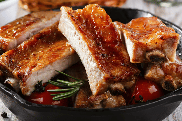 Recetas de cerdo con costillas doradas y glaseadas, acompañadas de salsa de tomate y romero.